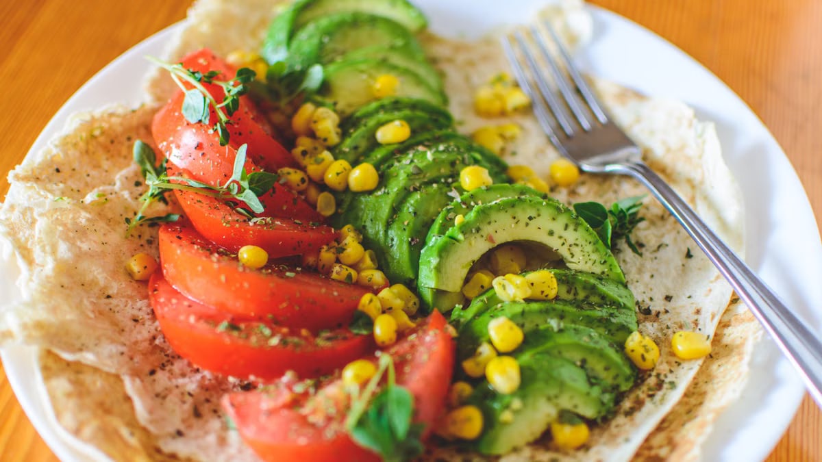 A vibrant salad with avocado, tomato, and corn on flatbread, topped with herbs, perfect for a healthy meal.
